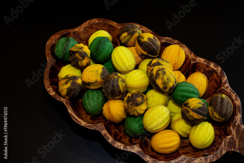 Multicolored nut-shaped cookies with filling on a wooden tray on a black background