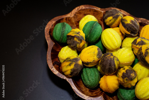 Multicolored nut-shaped cookies with filling on a wooden tray on a black background