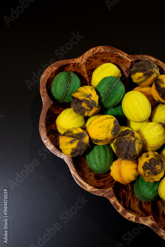Multicolored nut-shaped cookies with filling on a wooden tray on a black background