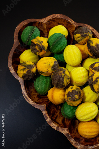 Multicolored nut-shaped cookies with filling on a wooden tray on a black background