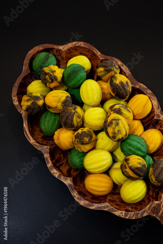Multicolored nut-shaped cookies with filling on a wooden tray on a black background