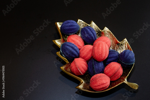 Red and blue nut-shaped cookies with filling on a golden leaf-shaped plate on a black background