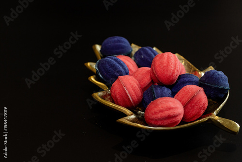 Red and blue nut-shaped cookies with filling on a golden leaf-shaped plate on a black background