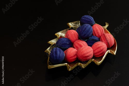 Red and blue nut-shaped cookies with filling on a golden leaf-shaped plate on a black background