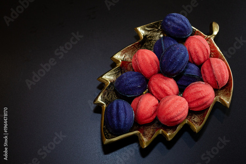 Red and blue nut-shaped cookies with filling on a golden leaf-shaped plate on a black background
