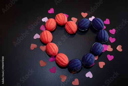 Heart shape made from baked nuts with filling on a black background with multi-colored paper hearts