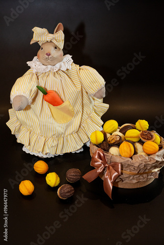 A full basket of multi-colored baked nuts against the backdrop of a bunny with a carrot in a beautiful dress on a black background