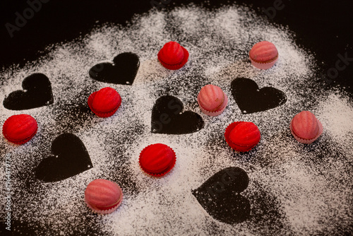 Pink and red baked nuts with filling on a black table sprinkled with powdered hearts