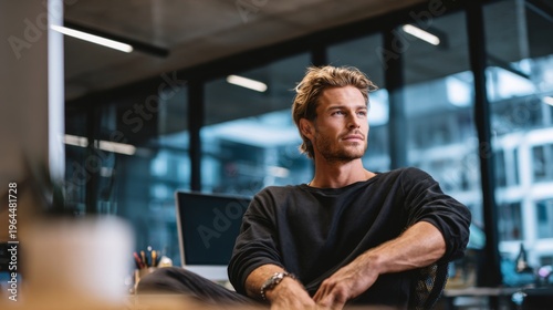 Thoughtful young man in modern office setting looking out of window, contemplating ideas for creative projects and personal goals