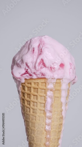 4K vertical video Melting strawberry ice cream scoop in waffle cone with dripping cream texture Close-up dessert showing freshness and summer heat.