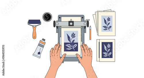 An overhead view captures two hands carefully placing a botanical design onto a printing press, surrounded by a roller, ink tube, coffee cup, pen, and stacks of paper.