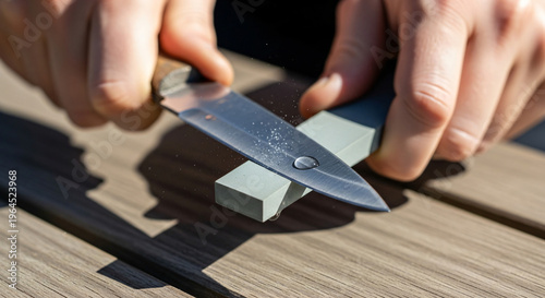 Person sharpening knife with whetstone on wooden surface  