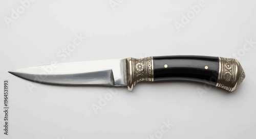 A sharp, stainless steel knife with a black handle, ornate metal accents, and a gray background