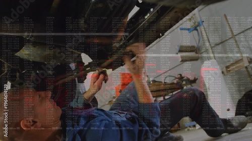 Auto mechanic lying under car finding bolt, using ratchet, repairing car while code overlay showing