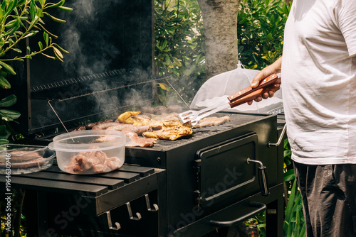 Canvas-taulu Backyard barbecue grilling meat on smoker with tongs
