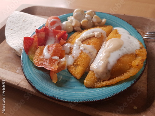 Fried fish cake with sour cream and vegetables in a blue plate