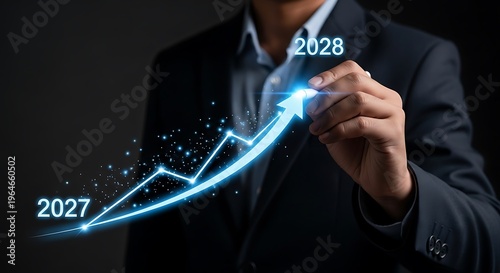 Businessman a glowing blue upward trend line graph with years 2027 and 2028 on a dark background suit