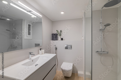 Modern bathroom with a sleek design. Features a white vanity, mirror, shower, and toilet. Bright lighting enhances the clean aesthetic.