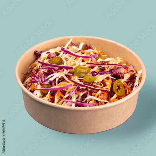 Fresh cabbage and carrot salad with red onion and jalapeno served in takeaway bowl on blue background