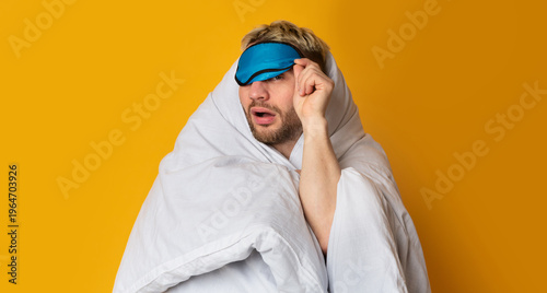 Foto Funny guy wrapped in blanket takes off his sleep mask and squints