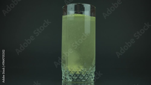 Effervescent Orange Vitamin Tablet Dissolving in Glass of Water. Close-up. Rising bubbles create a refreshing fizzy drink as the tablet gradually dissolves, turning the water into aт orange beverage