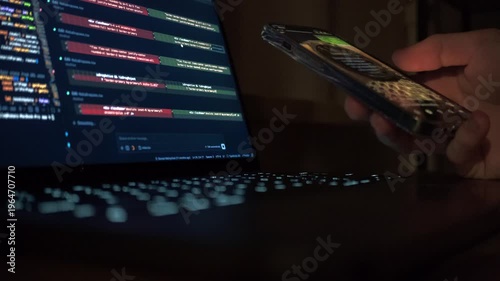 Programmer scrolling phone while AI generates code on laptop screen. Vibecoding with Claude Code