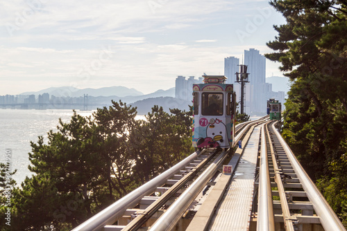 Фотография Colorful oceanfront capsule cars travel along an elevated coastal rail, offering scenic seaside views and a relaxed tourism experience over the water