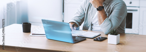 Принти на полотні Middle aged european businessman in glasses works on laptop at kitchen table