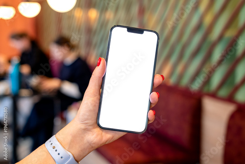 Hand holding smartphone mockup with blank screen in a modern cafe setting, blurred people working in the background
