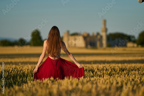 Woman rye field red dress. Happy woman in a long red dress in a beautiful cornfield. Old caste ruins in the background