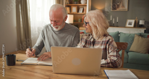 Bild auf Leinwand Elderly couple sits at a table with a laptop open, discussing life insurance