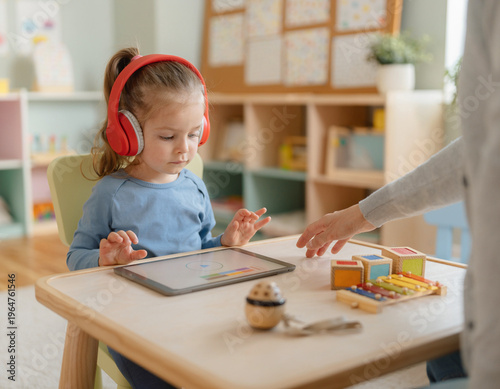 A child with red headphones listens to sound, focusing on auditory input for learning and sensory development. Early education for kids with developmental differences, exploring noise and sound.