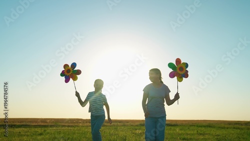 Photos Happy children girls playing with toy pinwheel outside in summer park