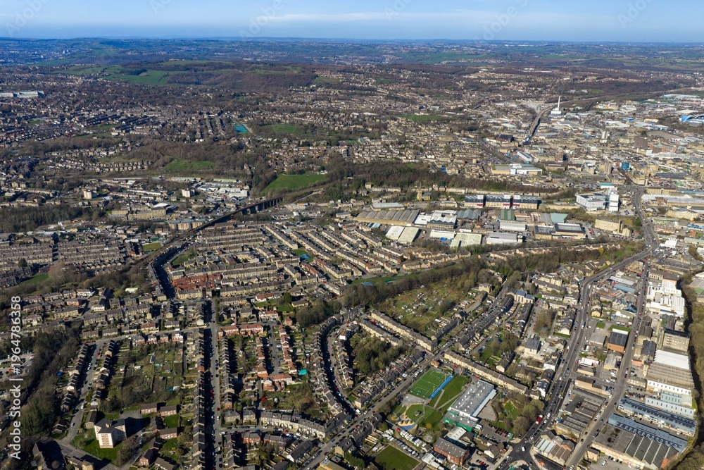 Obraz premium Aerial view of Huddersfield in West Yorkshire showing housing estates busy roads and industrial areas surrounded by green countryside in early spring with clear visibility across the landscape