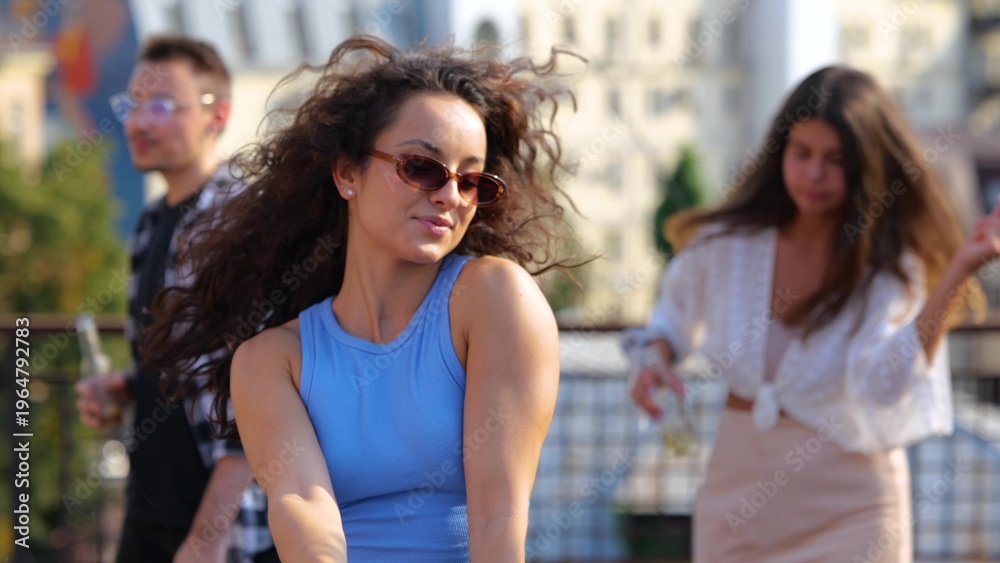 Obraz premium Close up of young brunette woman having fun with friends at sunset disco moving rhythmically to music. Pretty woman dancing at party outdoor on rooftop. Summer partying