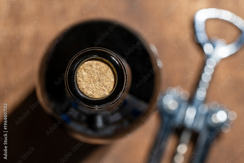 Fototapeta premium Closeup top view of dark glass wine bottle sealed with natural cork next to a metal corkscrew on a wooden background. Perfect for wine tasting and restaurant themes. Wine bottle with cork and opener
