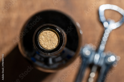 Closeup top view of dark glass wine bottle sealed with natural cork next to a metal corkscrew on a wooden background. Perfect for wine tasting and restaurant themes. Wine bottle with cork and opener