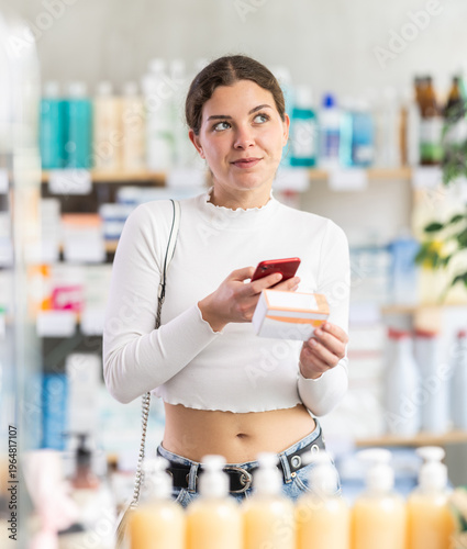 Young woman scans the barcode of a package with pills and medicines on her mobile phone, she reads the information on the pharmacy's website before buying