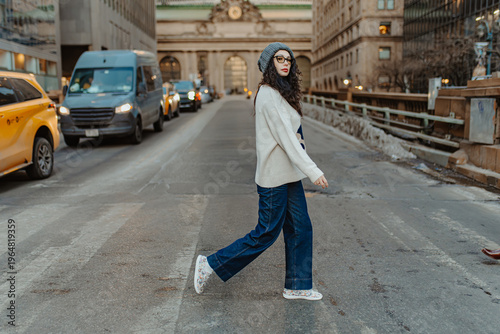 New York, USA, 25 December 2025: Woman walking across street with Grand Central Terminal background. Woman in casual winter clothes crossing road in front of historic train station building