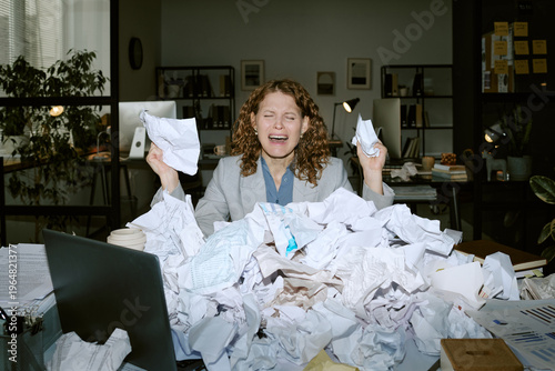 Konstfotografi Caucasian young woman sitting at cluttered desk holding crumpled papers, appeari