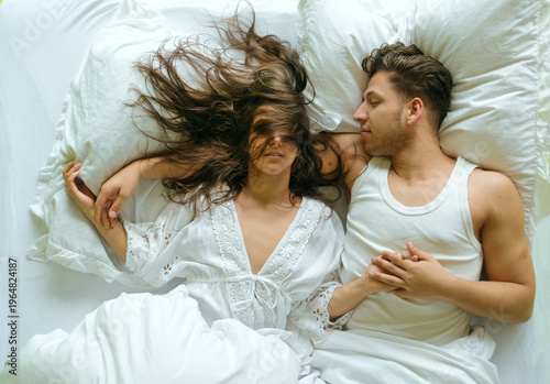 Young couple lying in bed holding hands woman hair flowing across face soft natural light creates intimate authentic moment of connection tenderness and quiet morning atmosphere