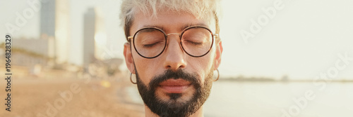 Fotografie Close-up of a young guy with glasses standing on the beach with his eyes closed