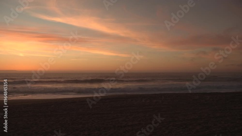 Waves breaking on beach at dusk with golden orange sky, wide angle view.