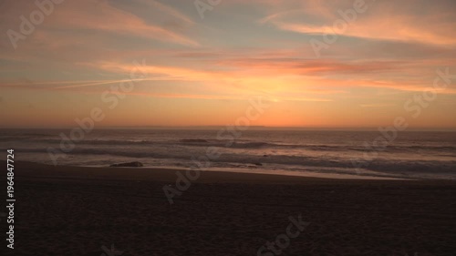 Wide angle view over beach at dusk, just after sunset, waves breaking on shore. 