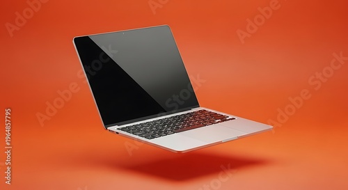 Silver laptop computer floating in mid air over a vibrant orange studio background with a blank black screen for digital mockup and technology