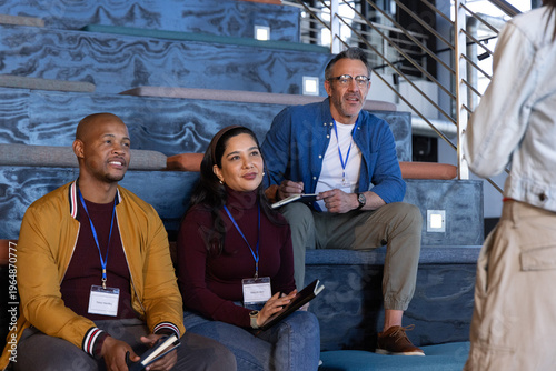 Diverse attendees sitting on tiered blue-marble steps listening and taking notes with lanyards