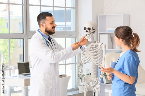 Male doctor and medical assistant examining skull of human skeleton in clinic