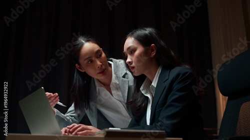 Two female colleagues discussing business project on laptop at night