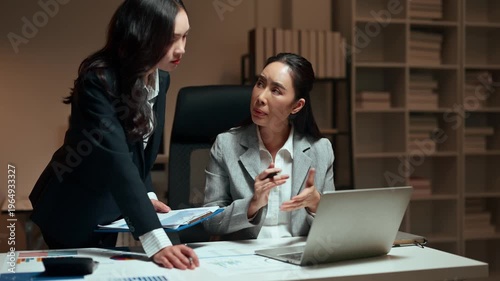 Asian businesswomen collaborating on project at night