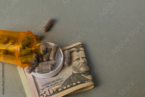 Money and medicine laying on a flat surface with pills spilled out of a bottle